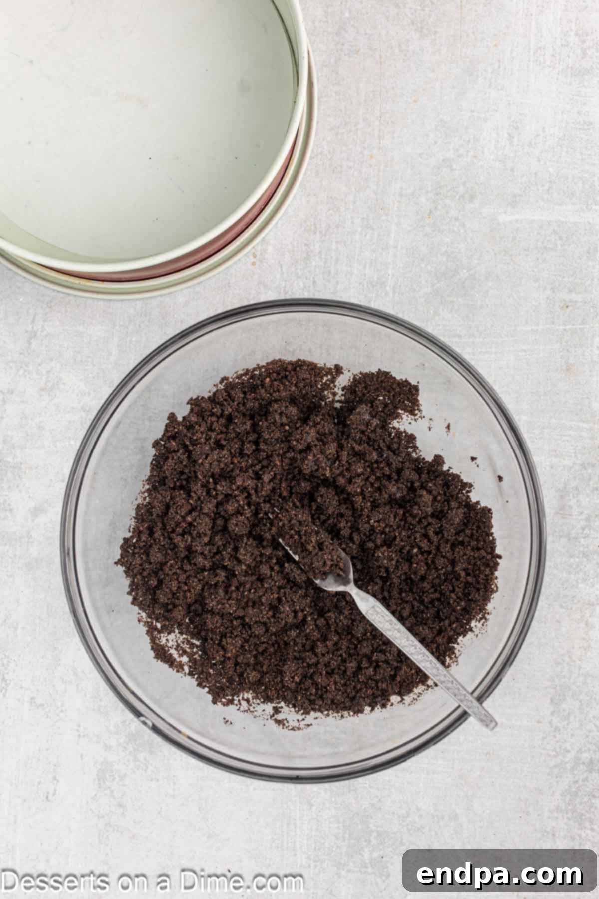 Oreo cookie crumbs mixed with melted butter in a bowl, ready to be pressed into a springform pan.