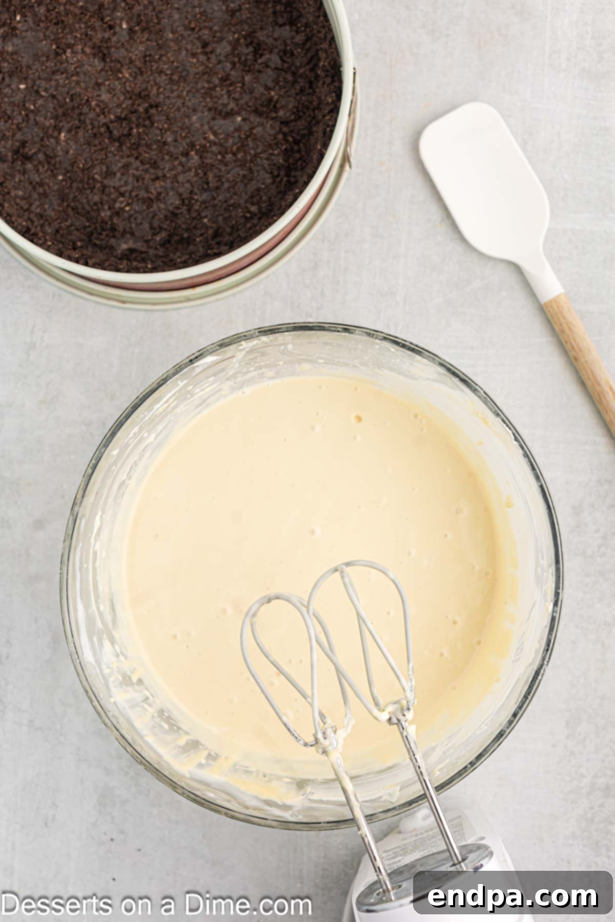 Eggs being slowly added one by one to the cheesecake batter in a mixing bowl.