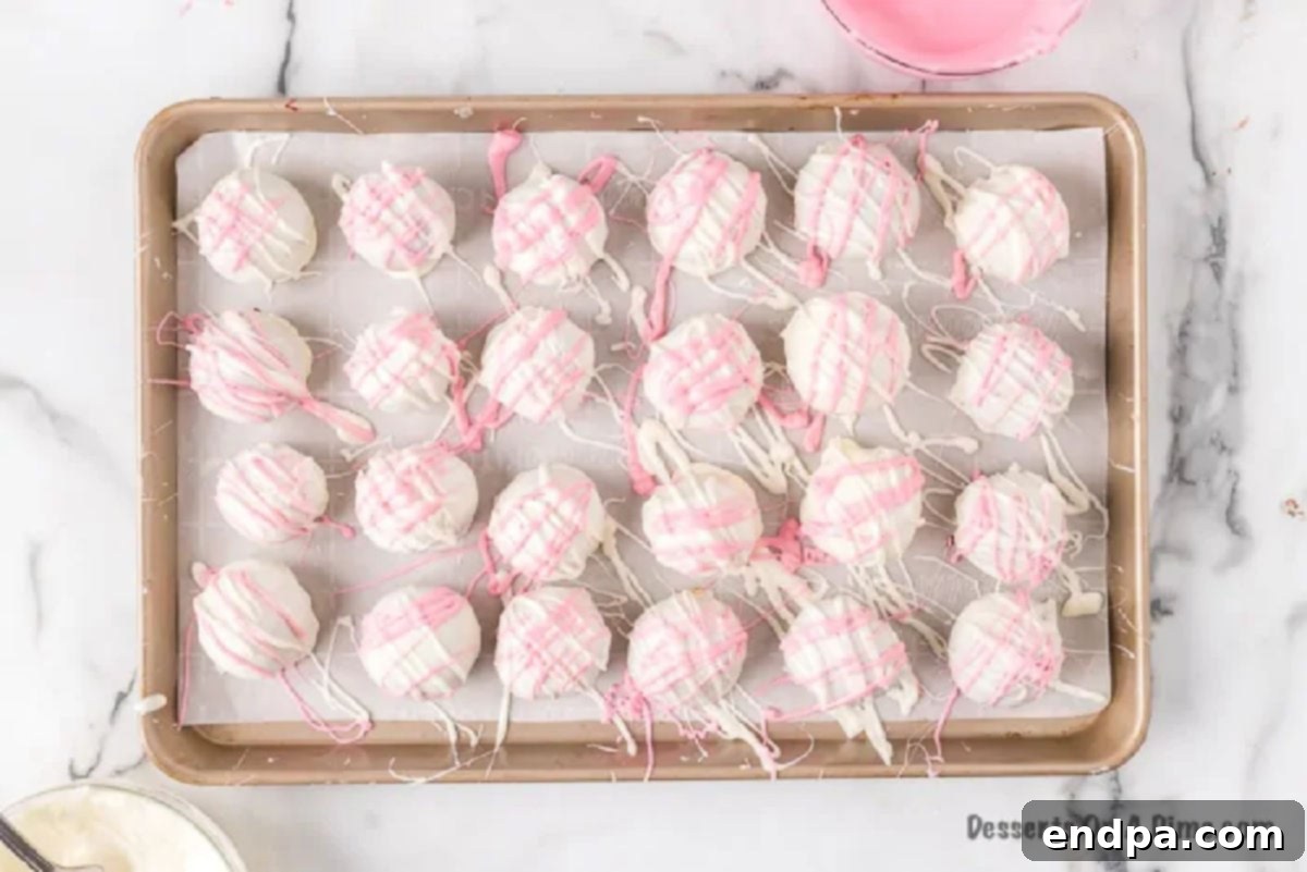 Red and pink candy melts being drizzled over white chocolate covered red velvet cake balls for decoration.