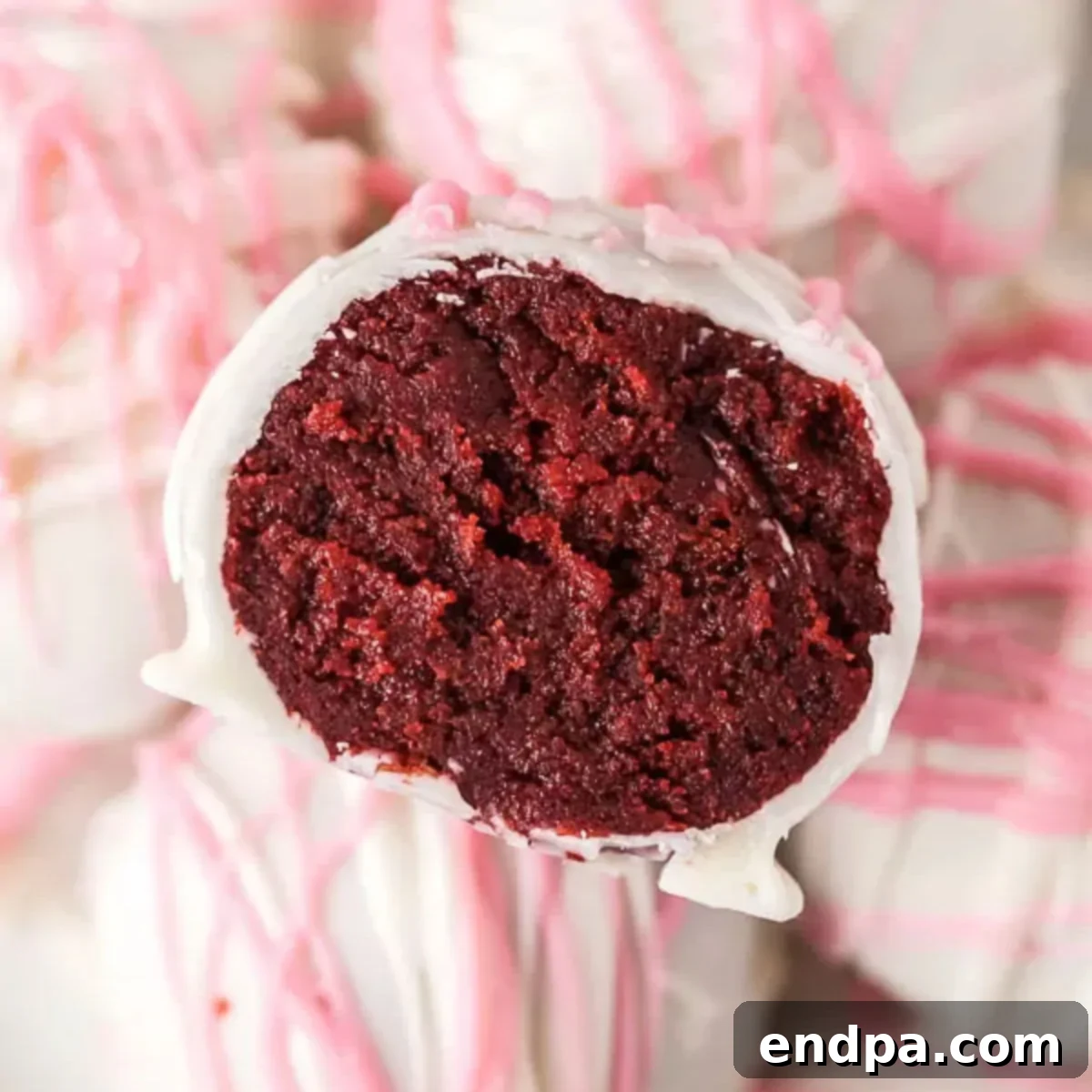 A perfectly round Red Velvet Cake Ball, covered in white chocolate and drizzled with pink and red candy melts.