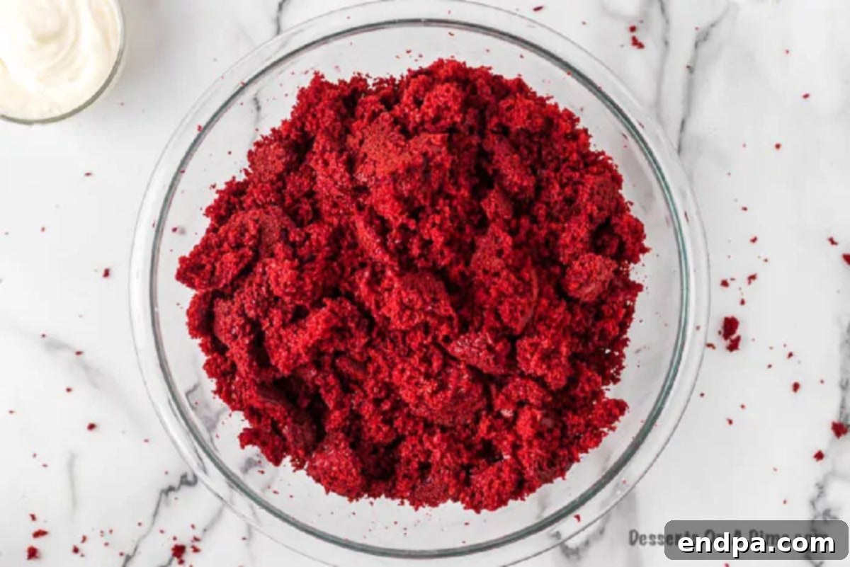Cooled red velvet cake being crumbled into a large mixing bowl.