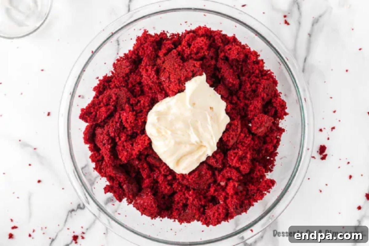 Cream cheese frosting being added to the crumbled red velvet cake in a bowl.