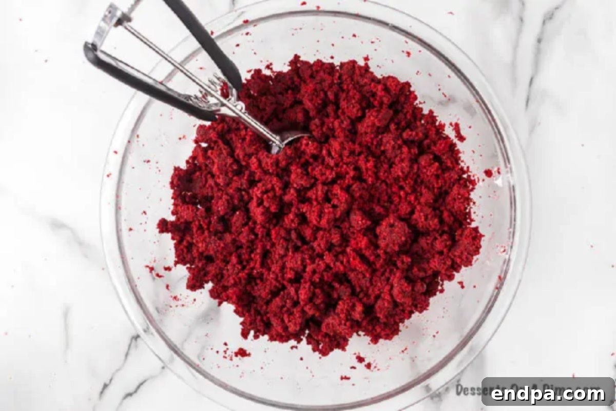 Hands rolling the red velvet cake and frosting mixture into uniform cake balls.