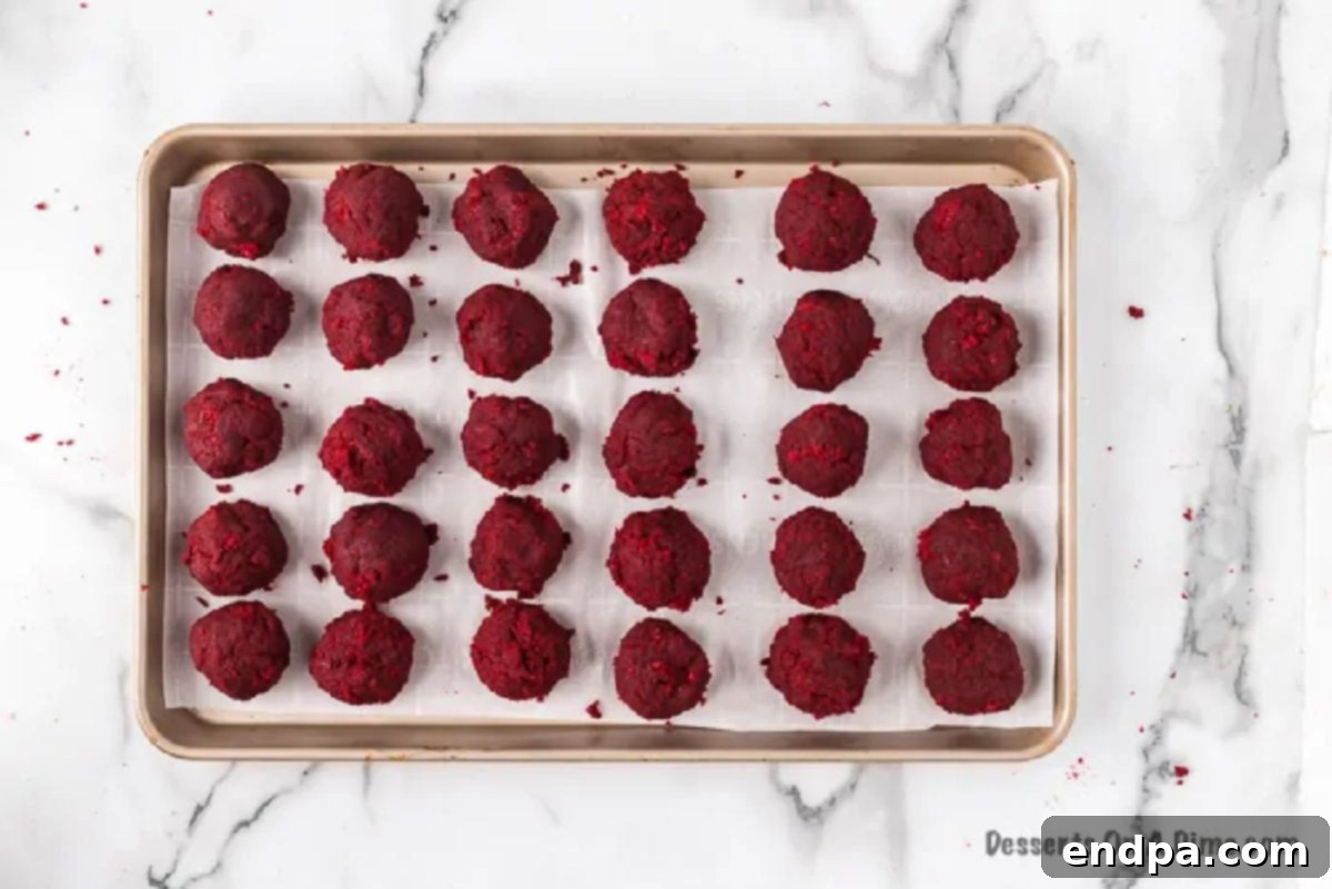 Red velvet cake balls arranged on a parchment-lined baking sheet, ready for chilling.