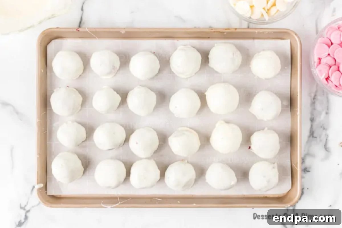 White chocolate coated red velvet cake balls setting on a baking sheet.
