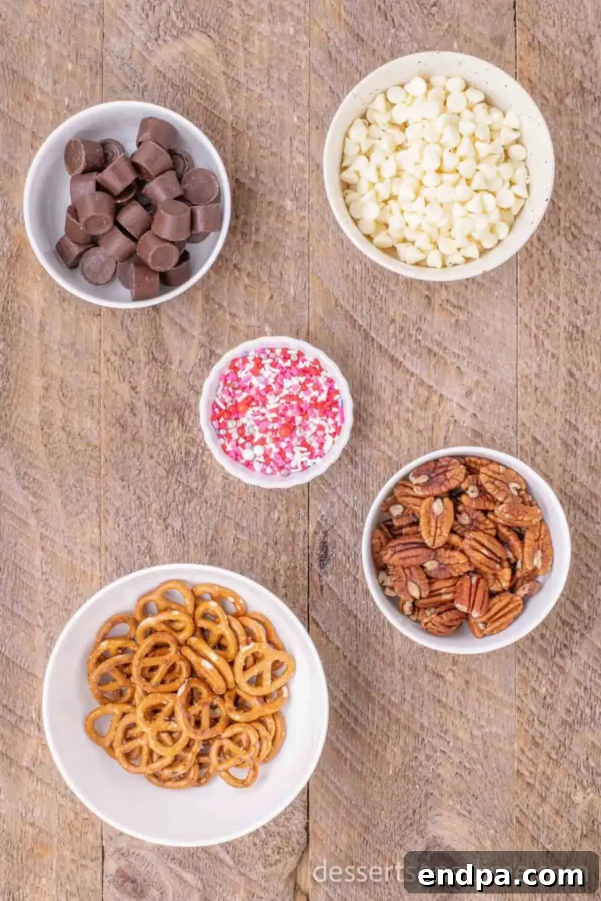 Collection of ingredients for Valentine's Day Rolo Pretzel Turtles including salted pretzels, Rolo candy, white chocolate chips, pecan halves, and colorful sprinkles.