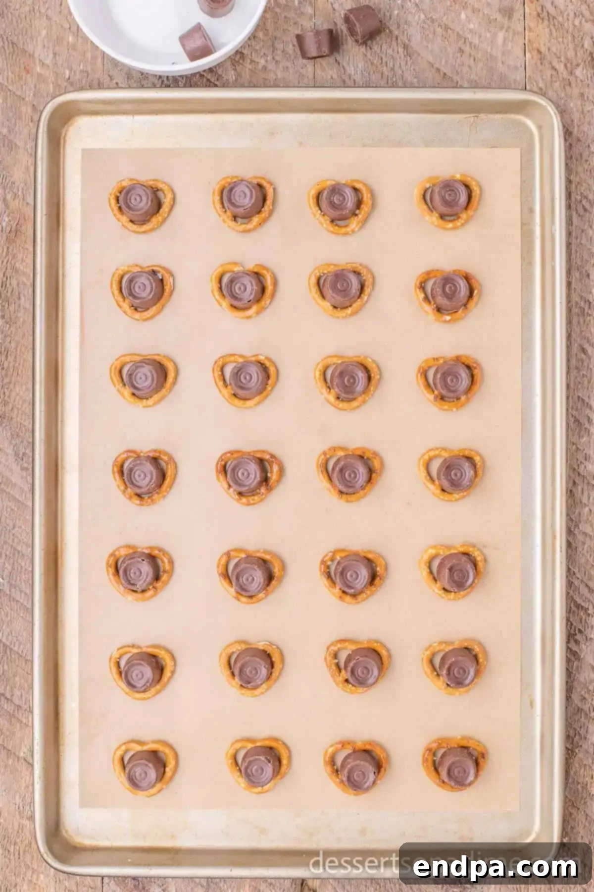 Salted pretzels topped with unwrapped Rolo candies arranged on a parchment-lined baking sheet, ready for the oven.