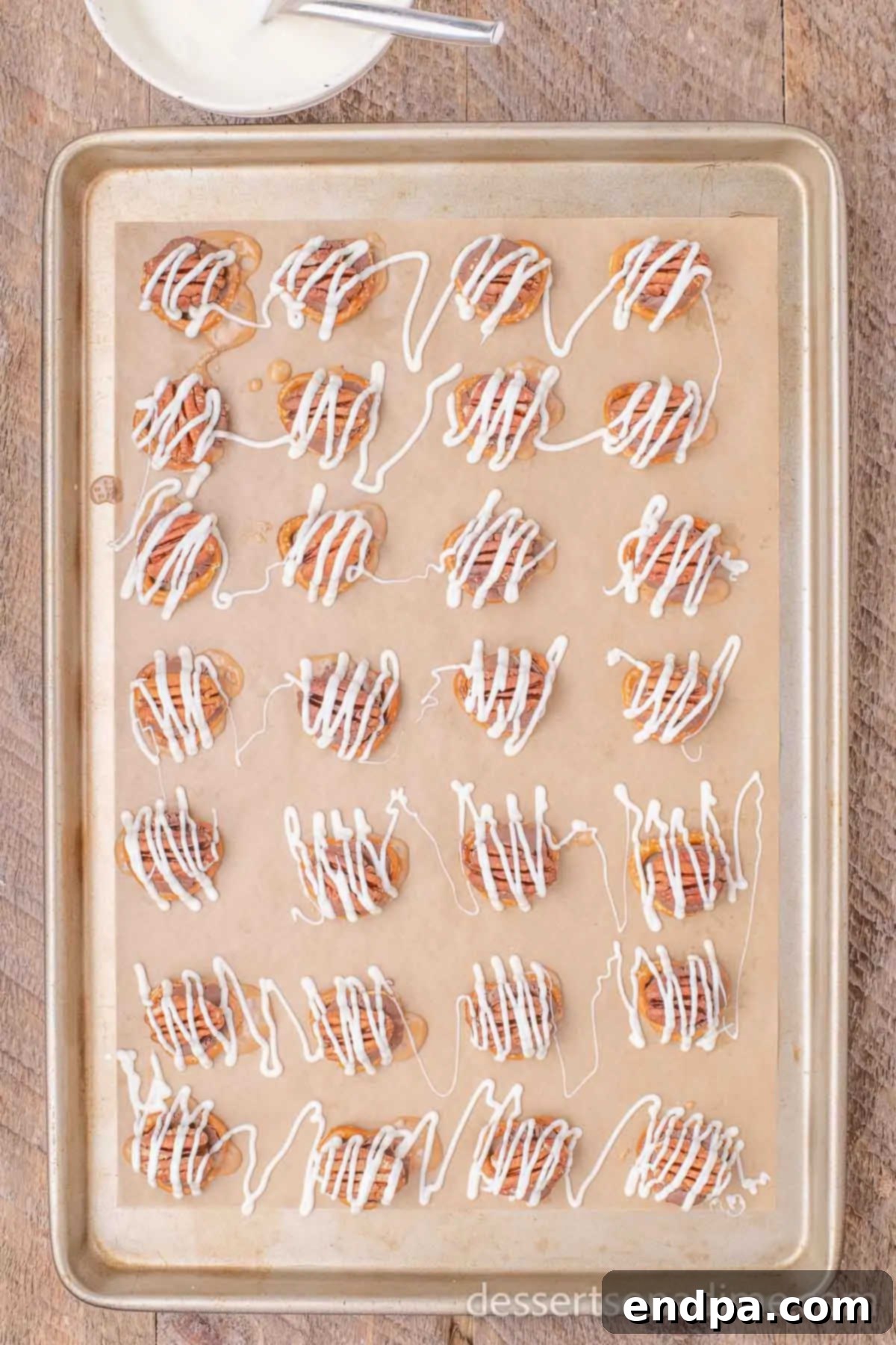 Melted Rolo candies on pretzels, with pecan halves pressed onto them, and a drizzle of melted white chocolate over the top.