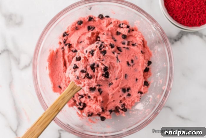 Mixing bowl with vibrant pink cookie batter and chocolate chips folded in, ready for baking.