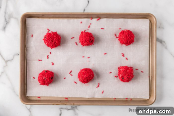 Dough balls covered in sprinkles and arranged on a parchment-lined baking sheet, chilling before baking.