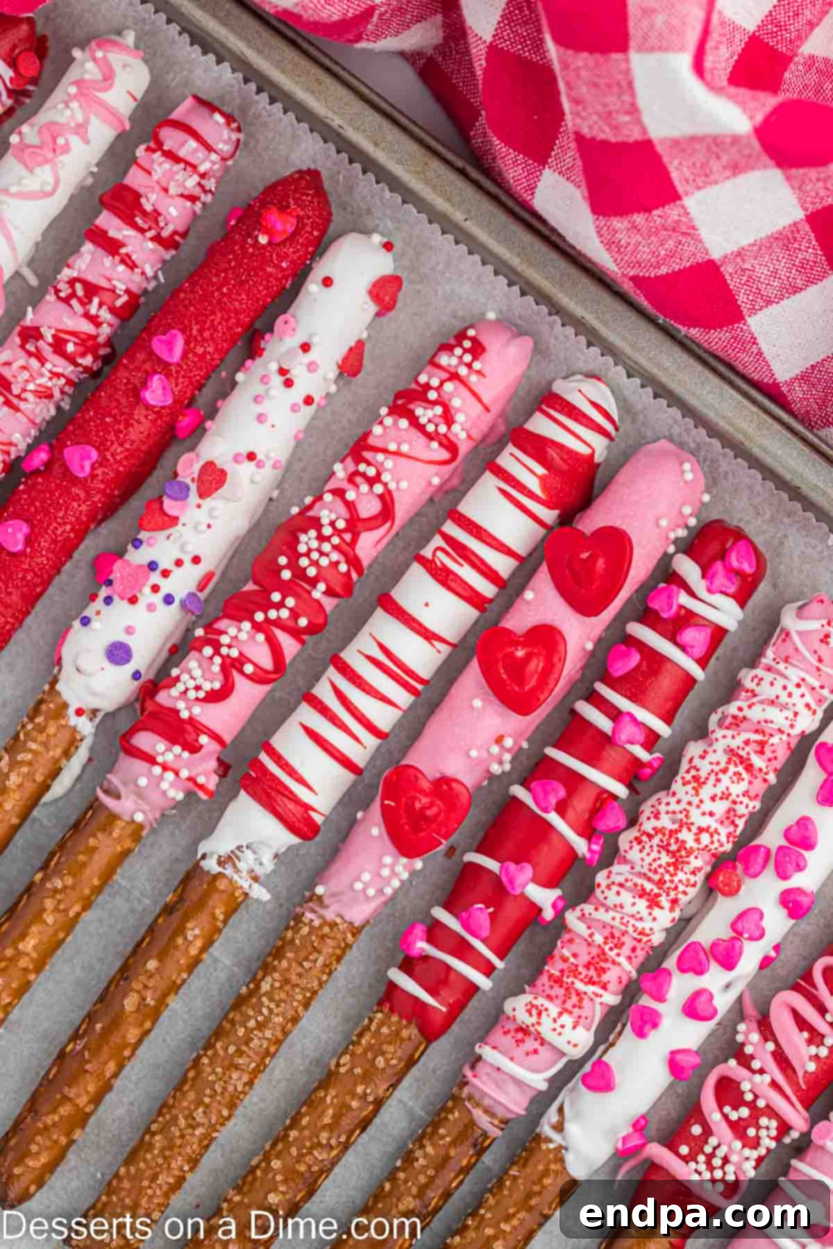 Valentine's Day Pretzel Rods on a baking sheet, decorated with pink, red, and white chocolate and sprinkles, ready to be enjoyed.