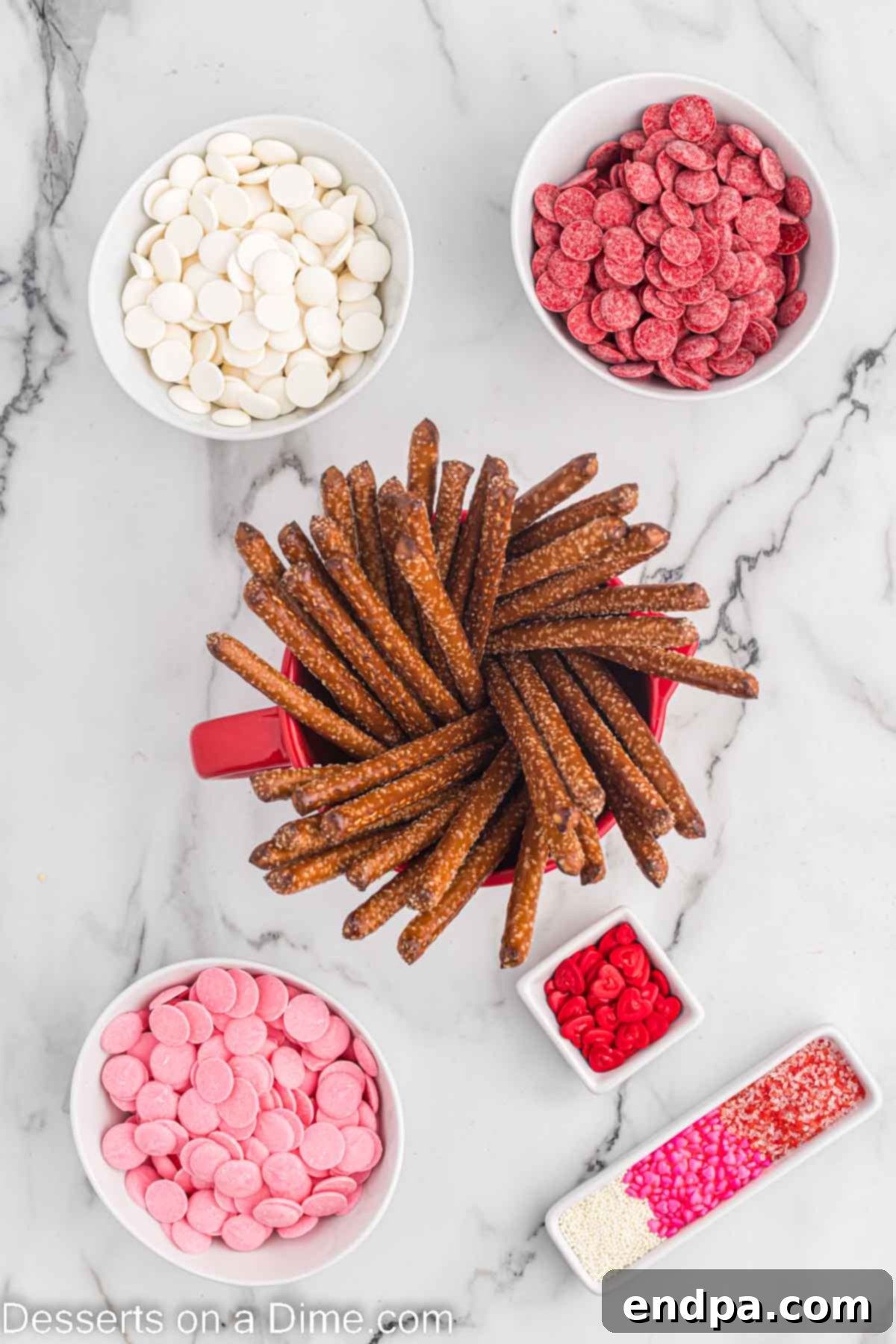 Ingredients for Valentine's Day Pretzel Rods: pretzel rods, pink, white, and red candy melts, and festive sprinkles laid out on a white surface.
