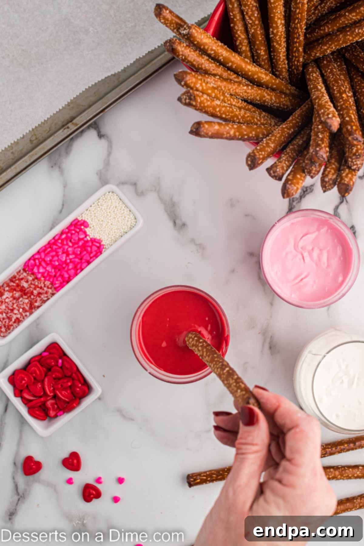 Melted candy wafers in jars with pretzel rods being dipped into them, showing the dipping process.