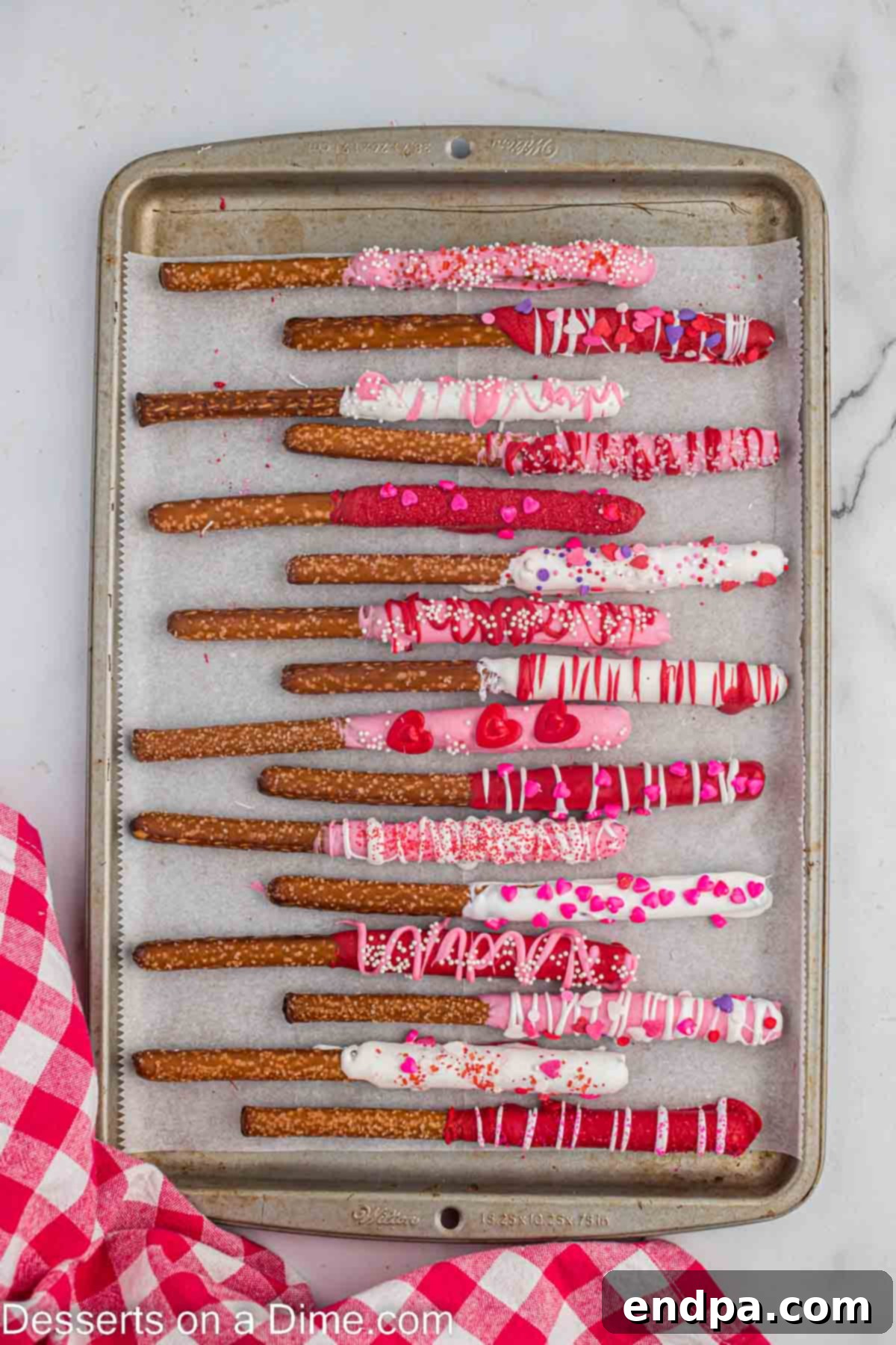 Dipped pretzel rods on a baking sheet, topped with melted wafers and candy, showcasing the decorated treats.