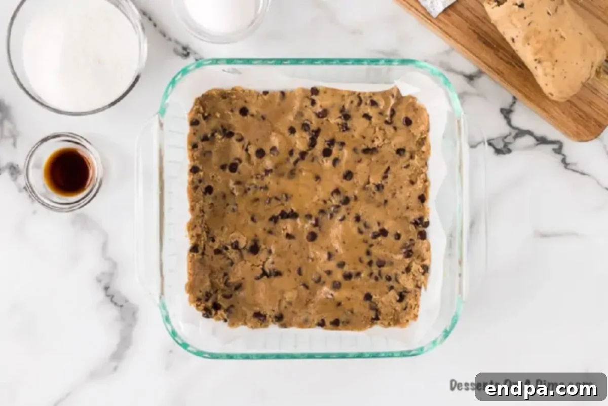 Half of the chocolate chip cookie dough pressed into the bottom of an 8x8 baking pan to form the crust.