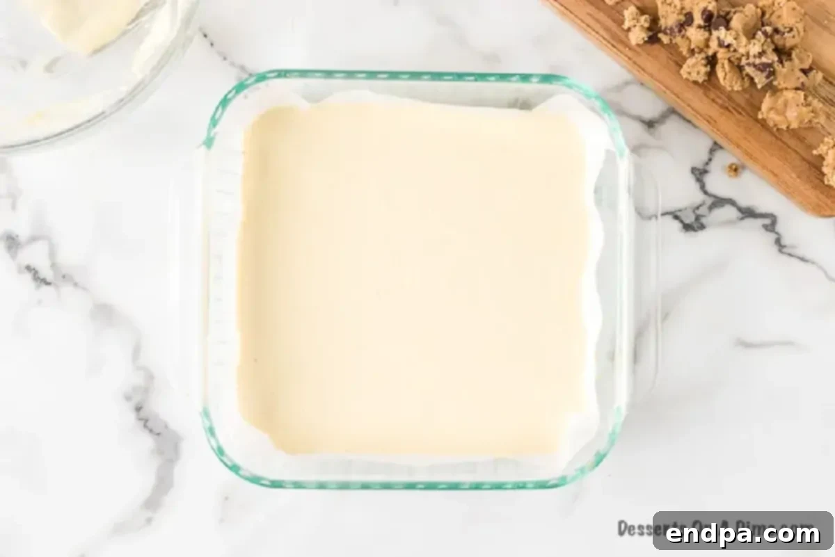 The smooth cream cheese mixture spread evenly over the chocolate chip cookie crust in the baking pan.
