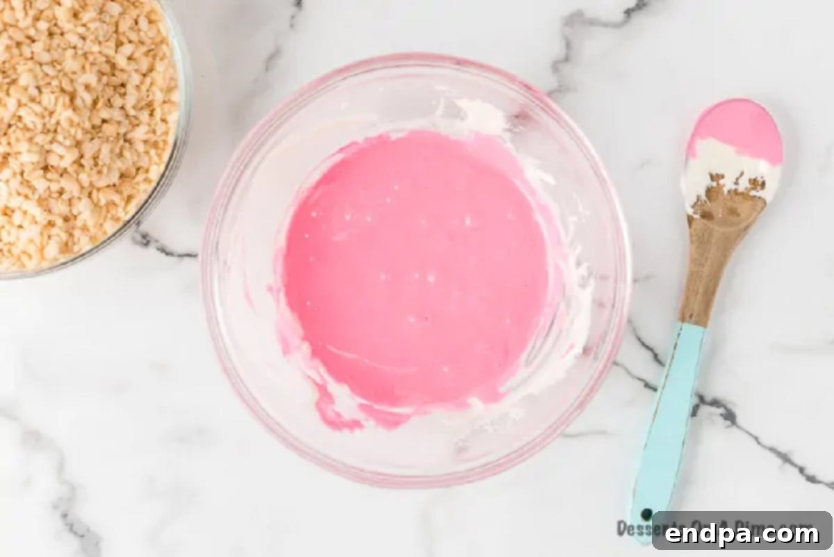 Pink food coloring being stirred into the melted marshmallow and butter mixture.