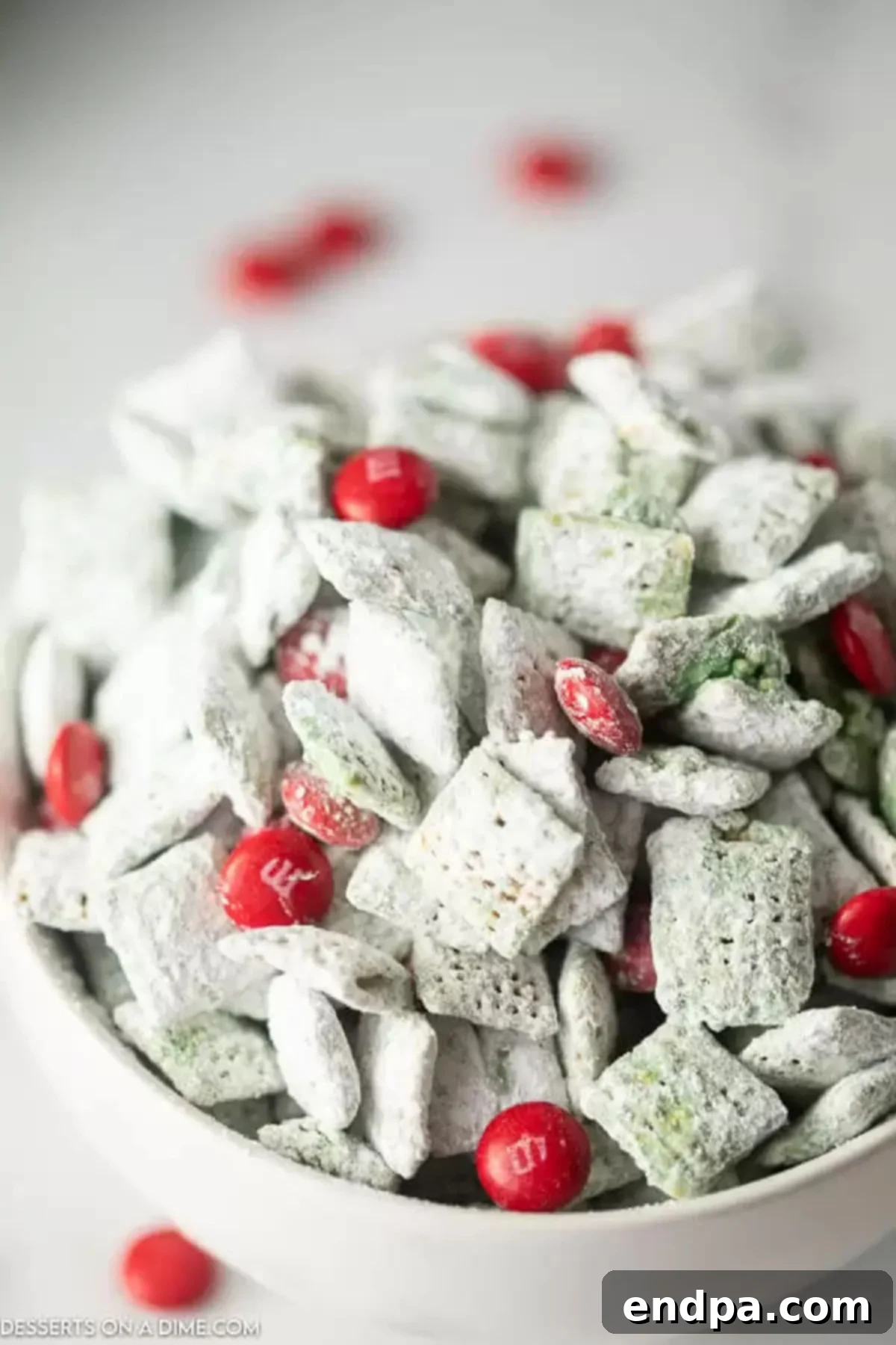 Whoville Christmas Crunch 2 Grinch puppy chow in a bowl, a festive green and red holiday treat, garnished with red M&Ms.