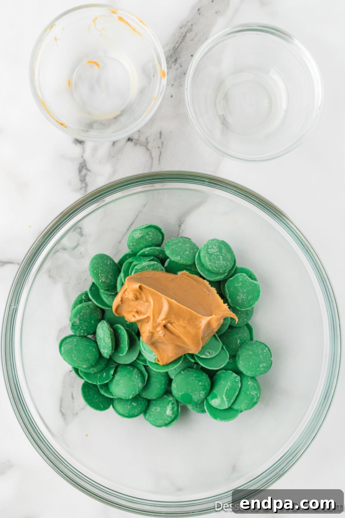 Whoville Christmas Crunch 4 Mixing bowl with creamy peanut butter and vibrant green candy melts, ready to be microwaved.