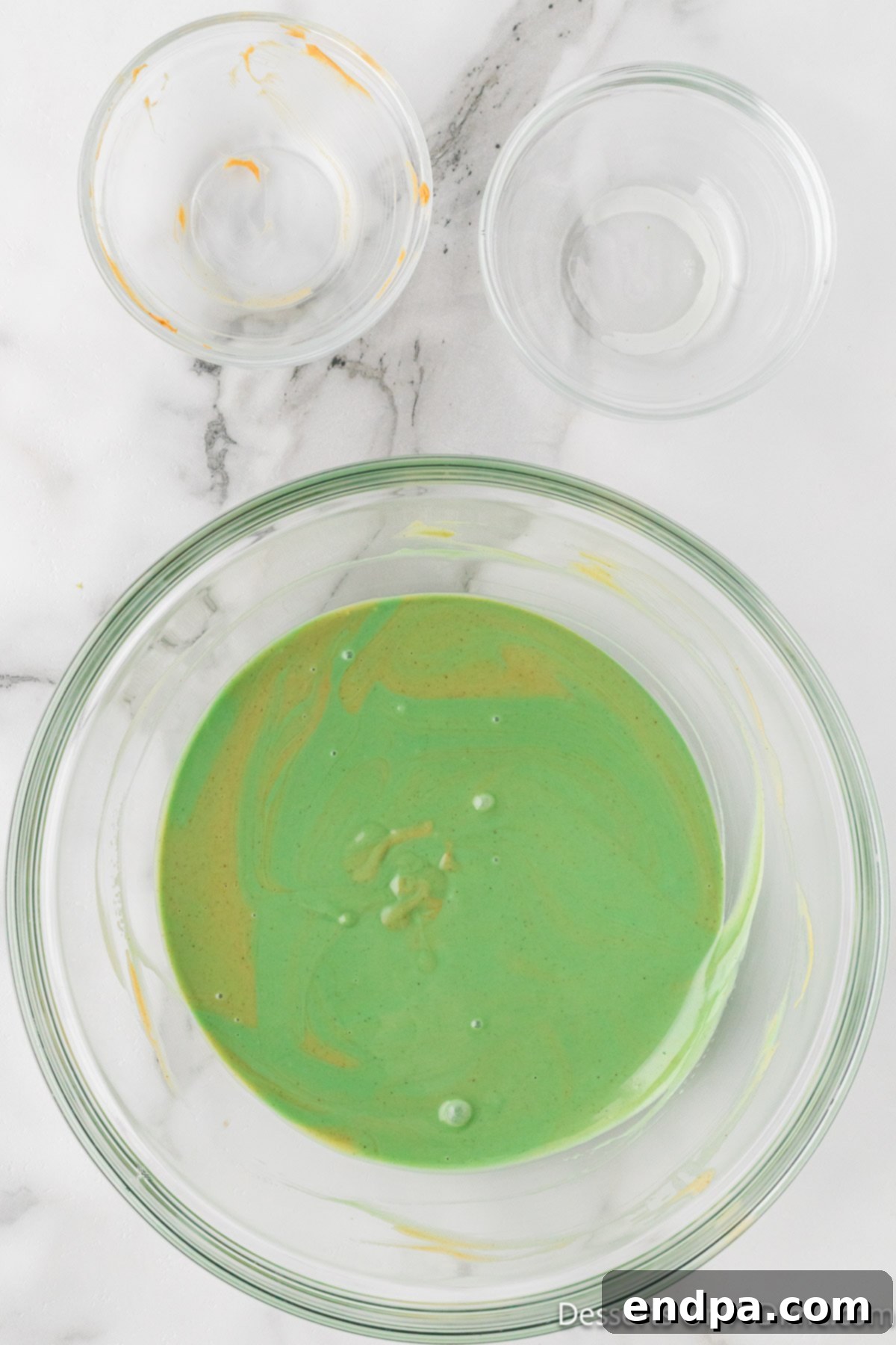 Whoville Christmas Crunch 5 Melted green candy melts combined with peanut butter in a bowl, forming a smooth and glossy mixture.