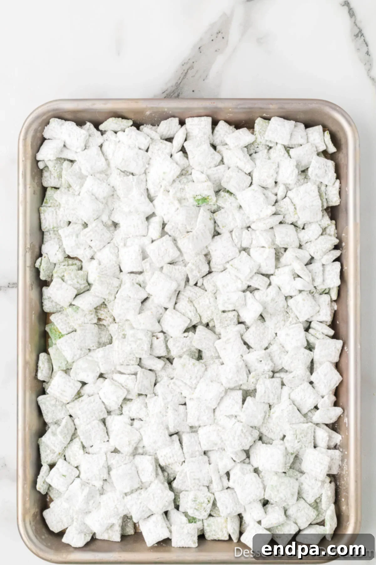 Whoville Christmas Crunch 8 Powdered sugar coated cereal spread out on a parchment paper lined baking sheet for cooling.