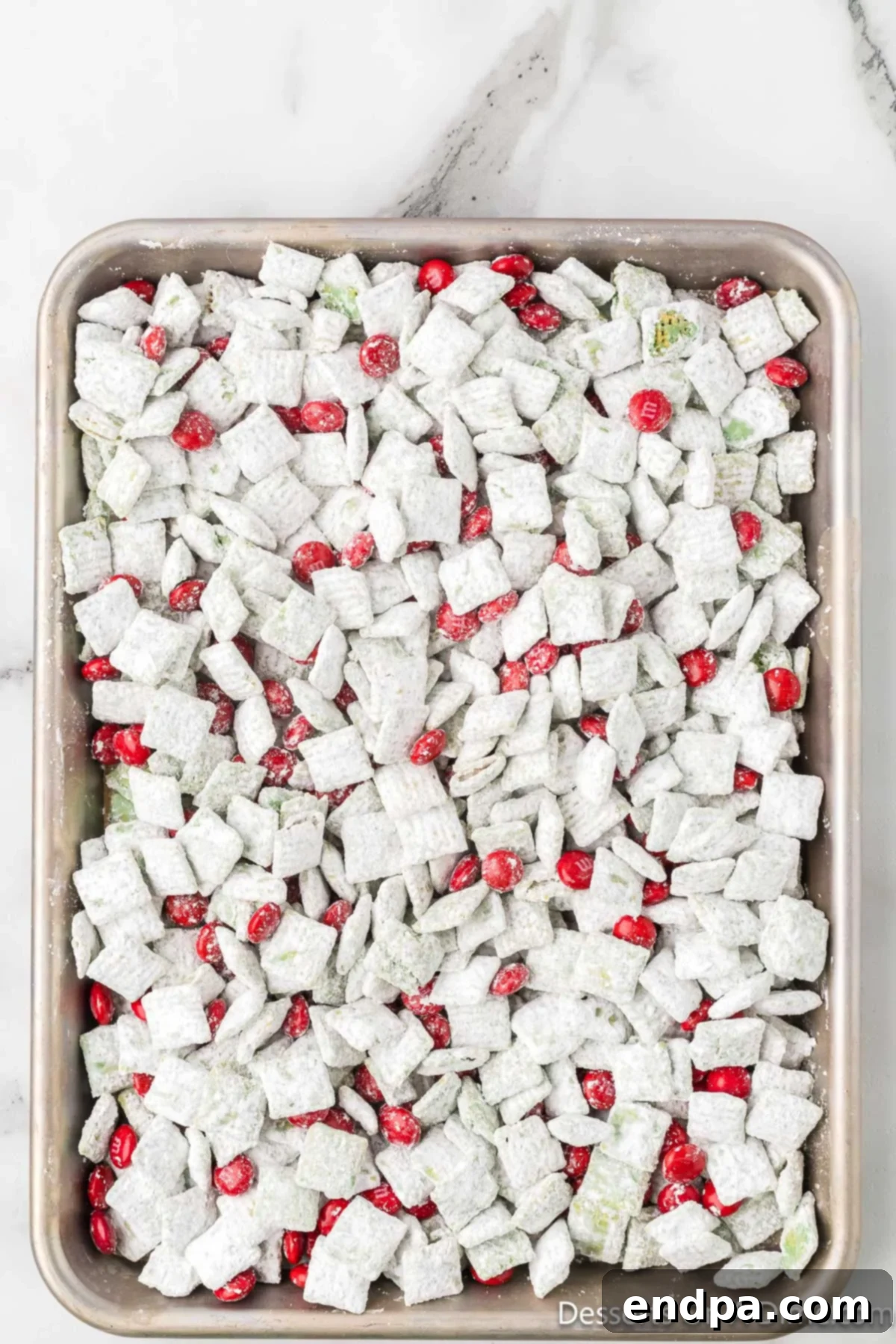 Whoville Christmas Crunch 9 Red M&M's generously sprinkled over the top of cooled Grinch puppy chow on a baking sheet.