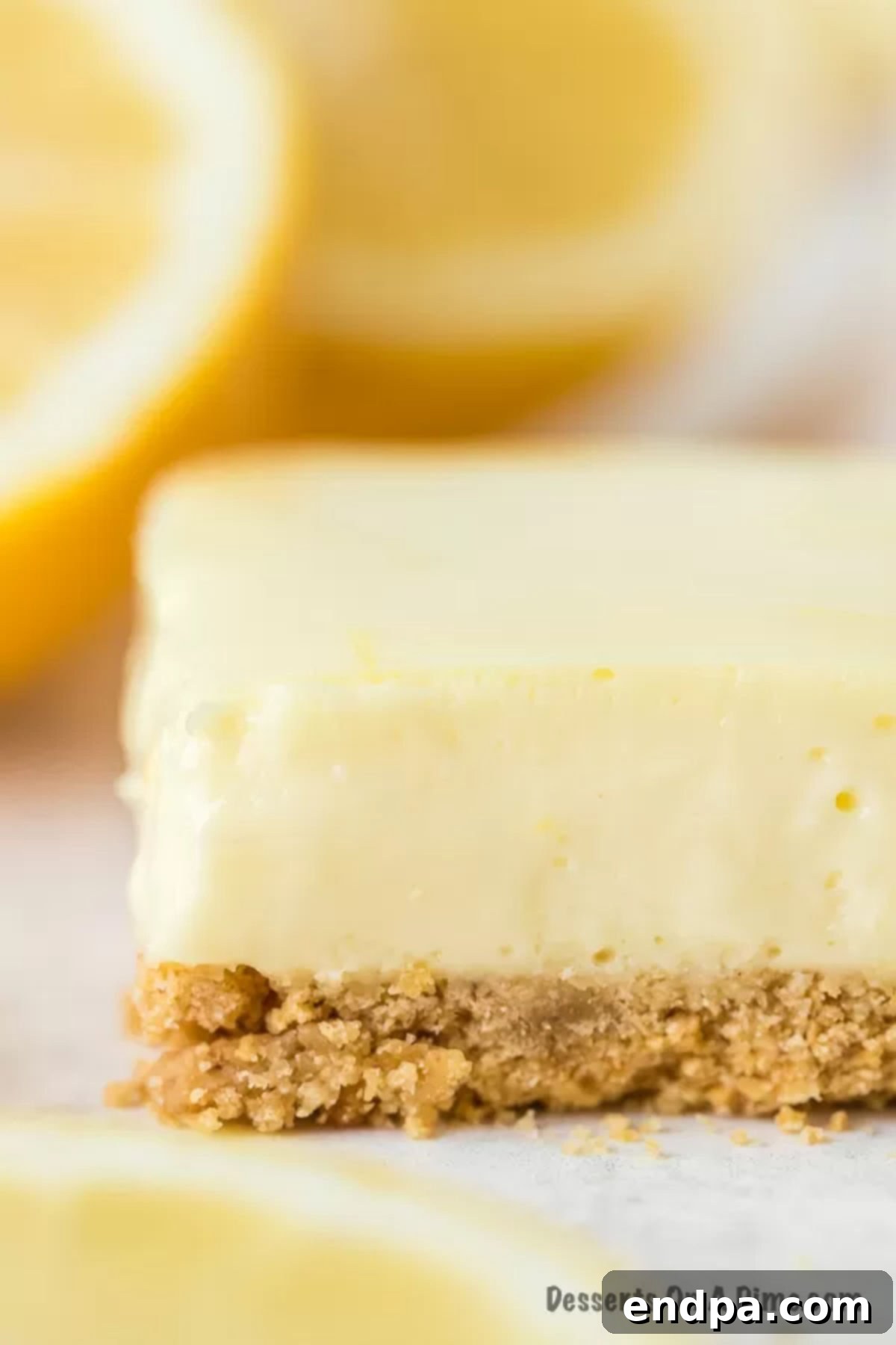 Zesty Lemon Cheesecake Bars 2 A lemon bar with fresh lemons in the background, showcasing the vibrant citrus and creamy texture.