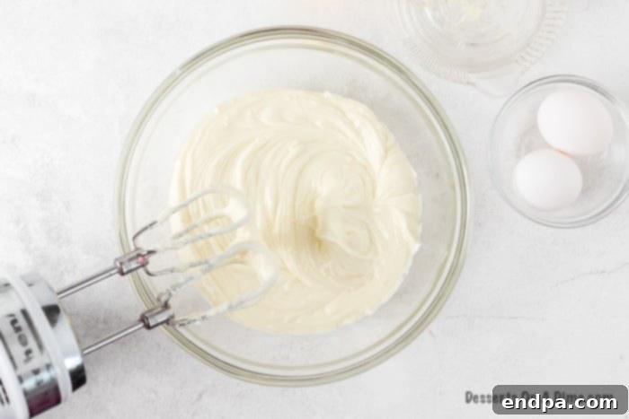 Zesty Lemon Cheesecake Bars 6 Cheesecake filling ingredients (cream cheese, sugar, lemon zest, lemon juice) combined in a bowl with a mixer, showing a smooth texture.