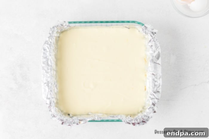 Zesty Lemon Cheesecake Bars 8 Cheesecake mixture spread smoothly over the graham cracker crust in the baking dish, ready for baking.