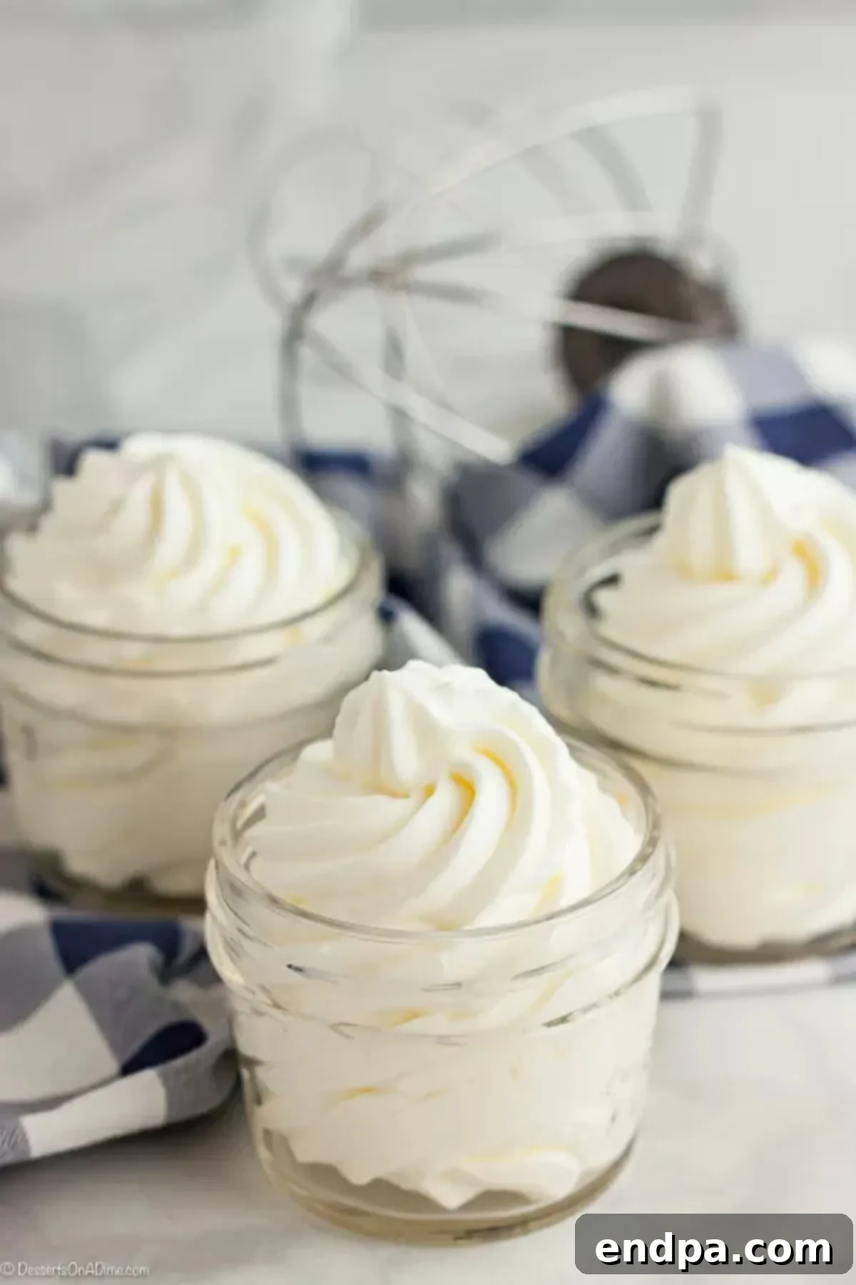 Once you try this Homemade Whipped Cream Recipe, you will never buy store bought whipped cream. This whipped cream recipes is easy with just 2 ingredients and tastes amazing. Try this heavy whipping cream recipes today. You will love this fresh whipped cream recipe! #dessertsonadime #whippedcream Homemade whipped cream in a small mason jar with 2 other jars and a whisk attachment behind it.