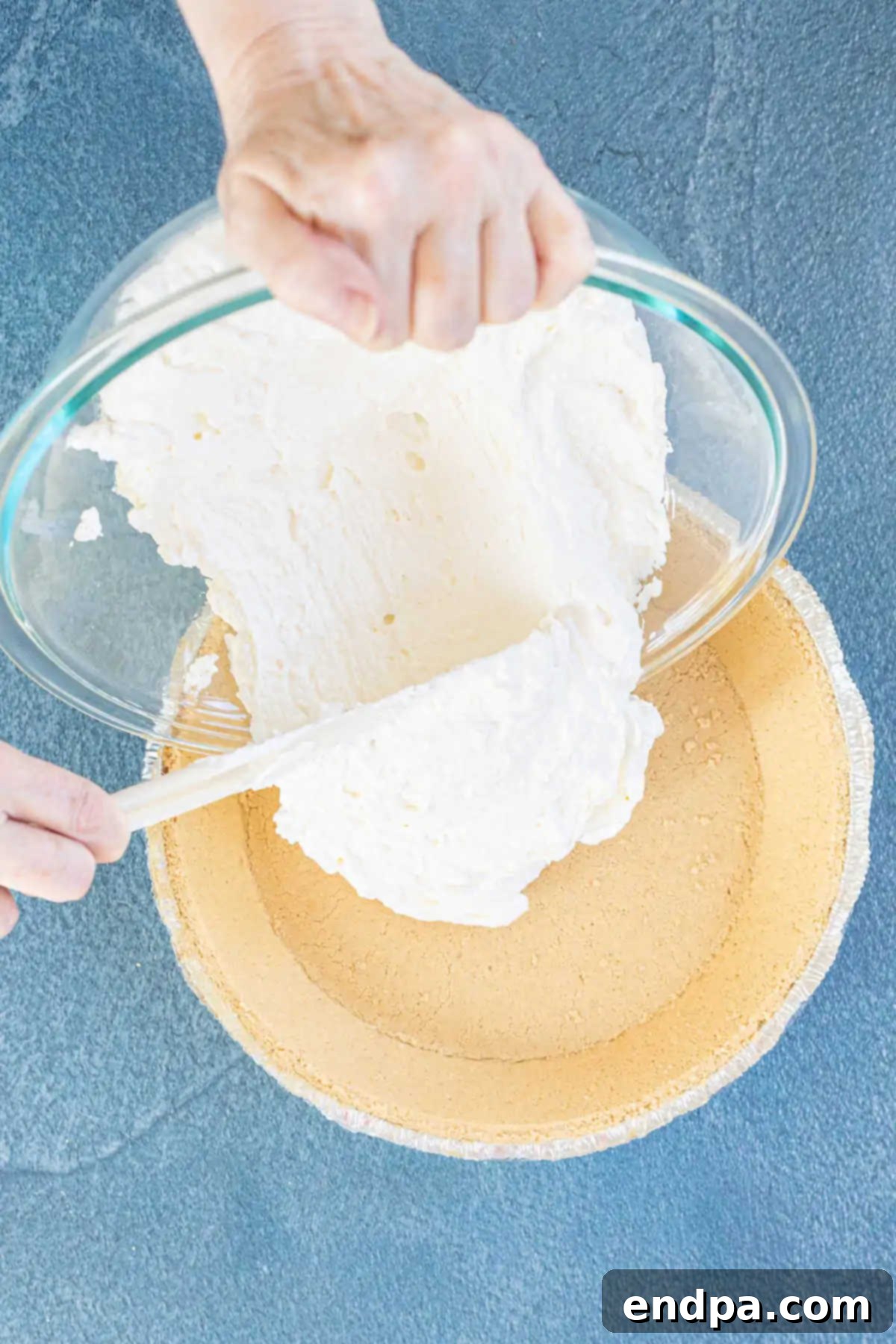 The creamy cheesecake mixture being spread evenly into a pie crust.