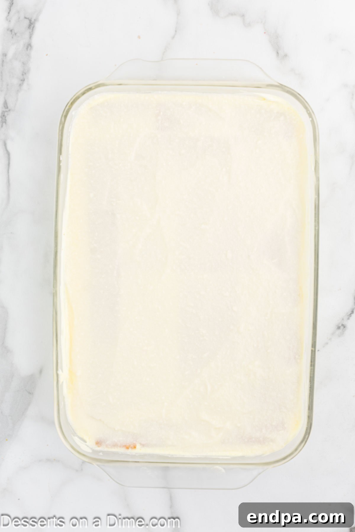 The smooth lemon frosting being spread generously over the top layer of the lemon icebox cake.