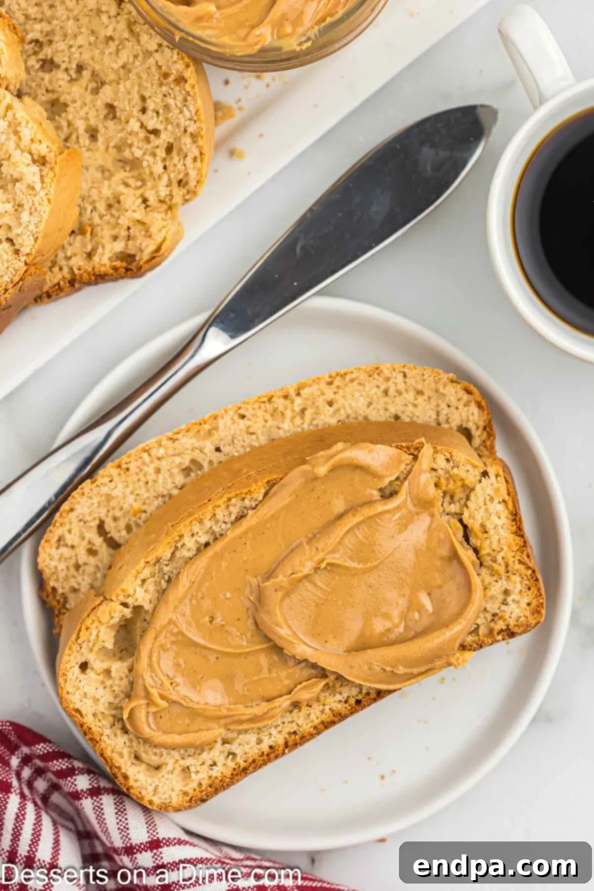 A golden-brown slice of freshly baked peanut butter bread, generously spread with creamy peanut butter, resting on a rustic wooden board.