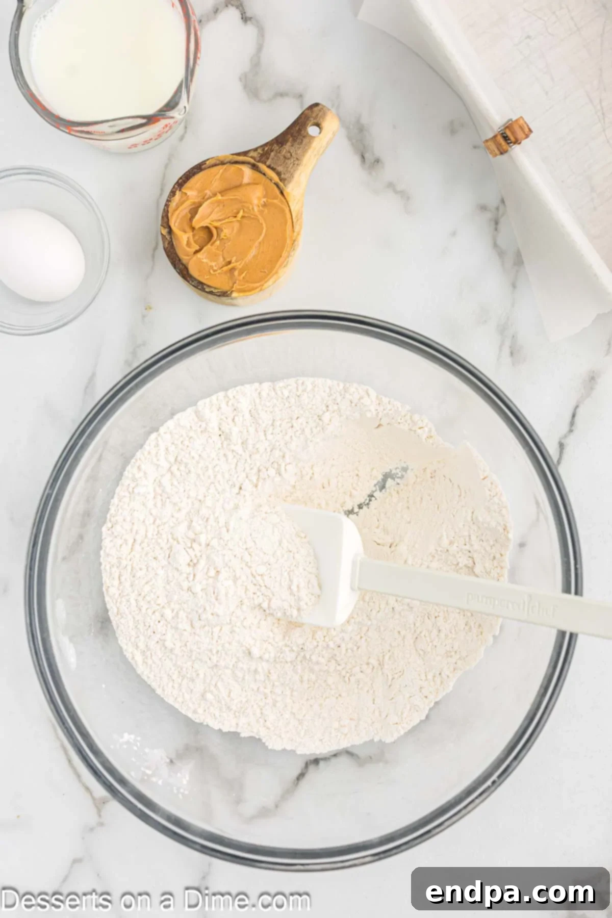 A large mixing bowl containing white flour, granulated sugar, and a spoonful of baking powder and salt, waiting to be whisked together.
