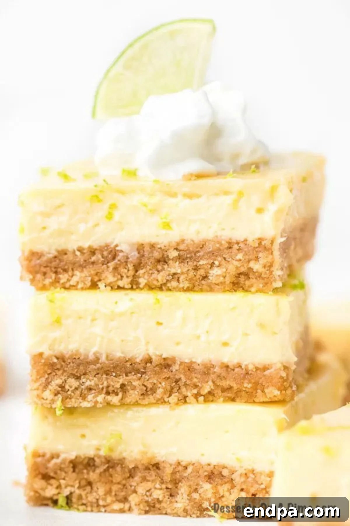 These decadent key lime bars are the perfect size for parties and more. The cream cheese filling is light and creamy with the best lime flavor. Try key lime bars easy and delicious with graham crackers crust. Key lime bars recipe is the best ever dessert and so easy. #dessertonadime #keylimebars Key Lime Bars stacked with fresh lime on top, showcasing a creamy texture and golden crust