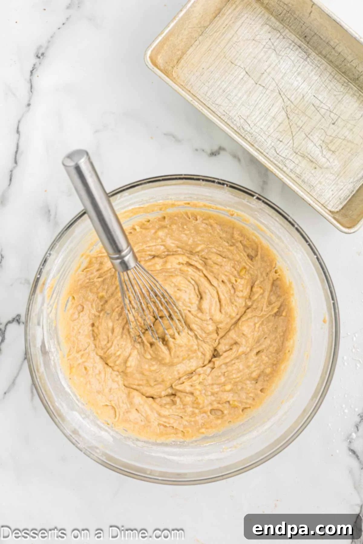 The flour mixture being gently whisked into the banana and wet ingredients in a mixing bowl.