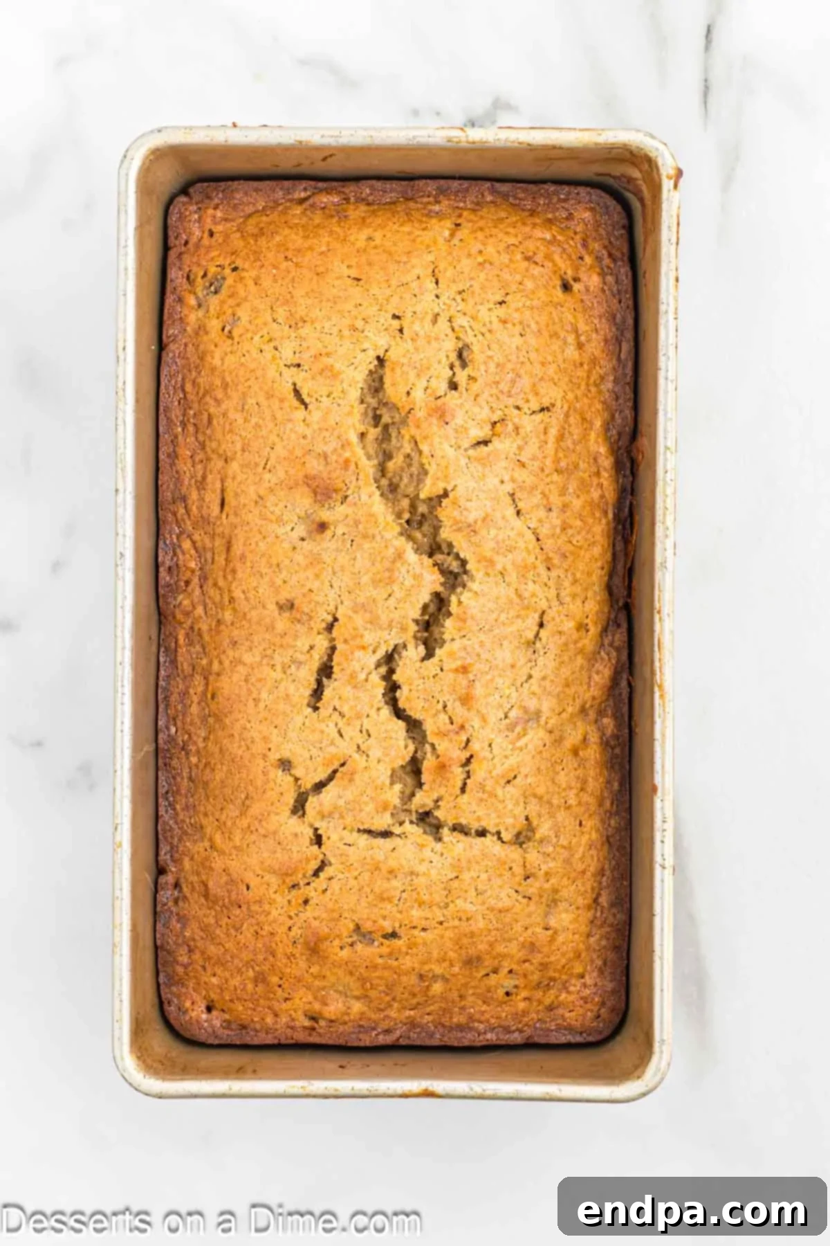 A freshly baked loaf of brown sugar banana bread cooling in its pan on a wire rack.