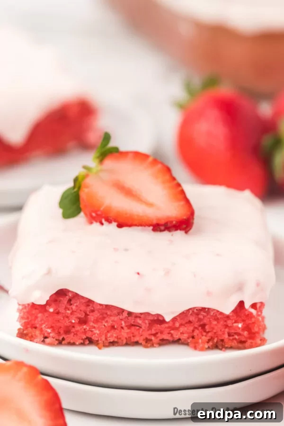 Strawberry sheet cake is so decadent with the best cream cheese frosting. No one will guess it all starts with a cake mix. A beautiful slice of strawberry sheet cake, topped with creamy pink frosting and fresh strawberry slices, presented on a white plate.