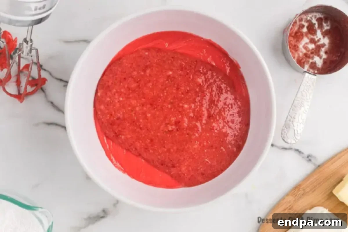 Effortless Strawberry Sheet Cake 3 Strawberry cake batter, a beautiful pink color, being mixed in a large white bowl with an electric stand mixer.