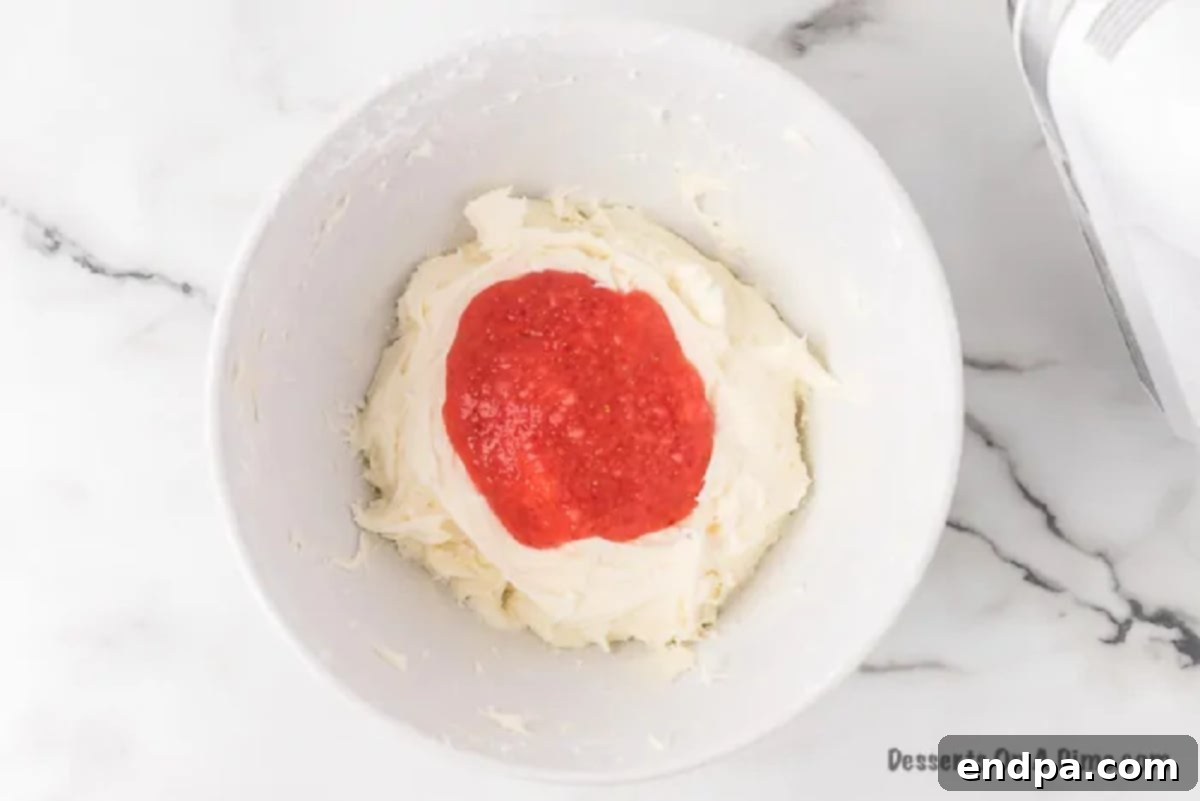 Effortless Strawberry Sheet Cake 6 Strawberry puree being folded into the smooth cream cheese frosting in a mixing bowl, creating a pink hue.