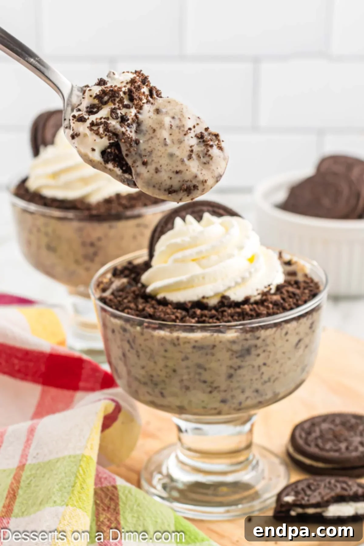 A single cup of homemade Oreo pudding, topped with a generous swirl of whipped cream and a chocolate drizzle.