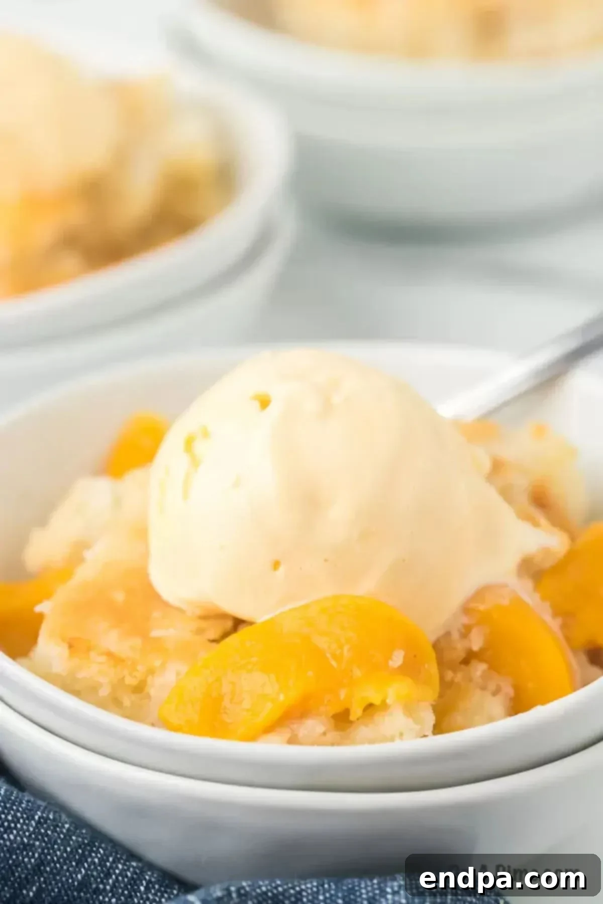 A serving of homemade peach cobbler in a bowl, perfectly topped with a scoop of melting vanilla ice cream.