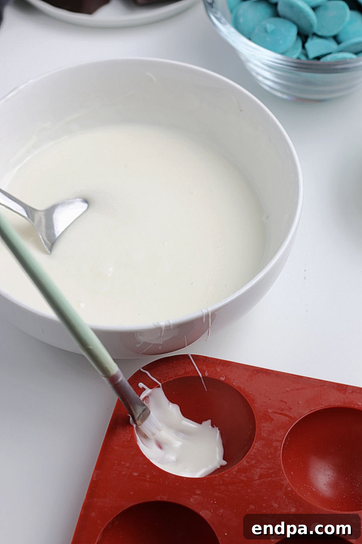 Melted chocolate being carefully applied to the inside of a silicone dome mold with a paintbrush.