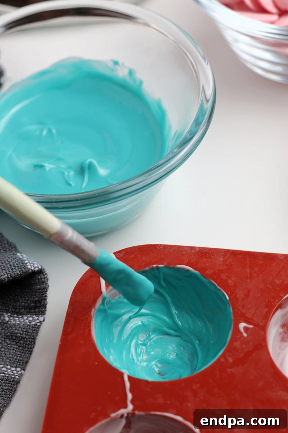 A paintbrush meticulously spreading melted chocolate evenly inside a silicone dome mold, ensuring no gaps.
