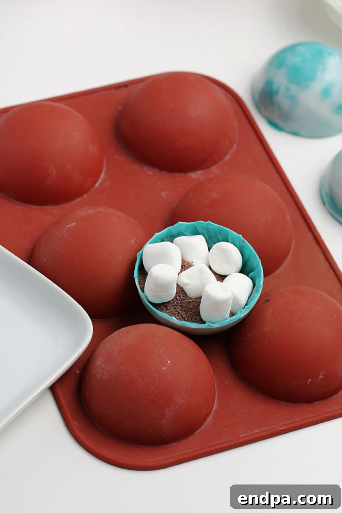 A chocolate half-sphere filled with hot cocoa mix and mini marshmallows, ready to be sealed.