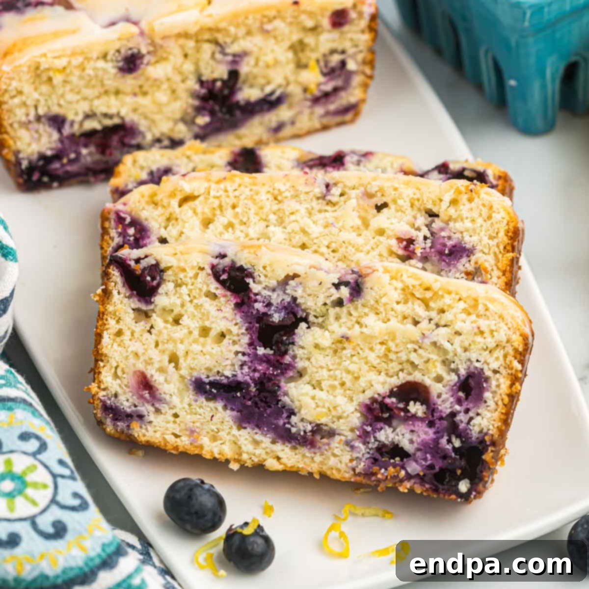 A freshly baked loaf of Lemon Blueberry Bread, drizzled with lemon glaze, ready to be sliced.