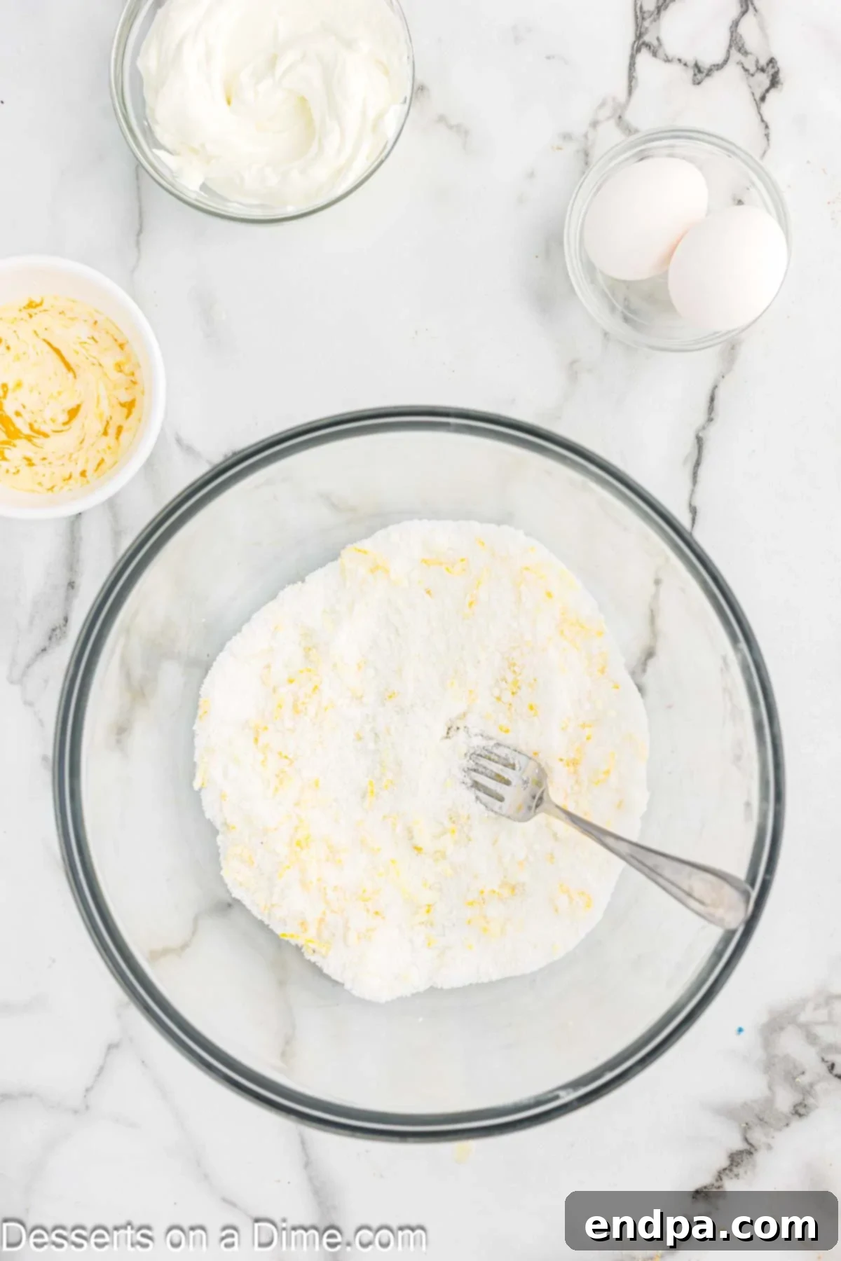 Mixing bowl with sugar and lemon zest being combined with a fork.
