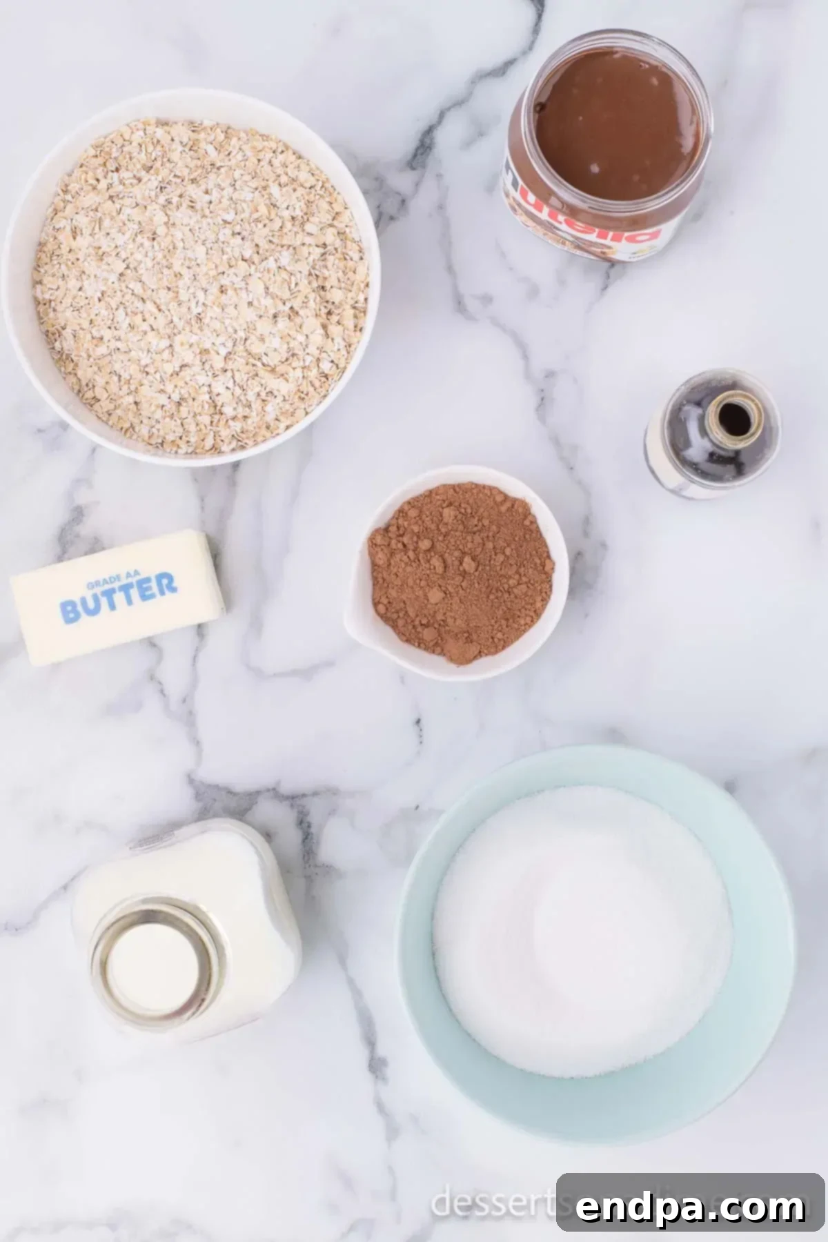 Ingredients for Nutella No Bake Cookies - butter, cocoa powder, milk, vanilla, Nutella and quick oats, laid out on a clean surface.