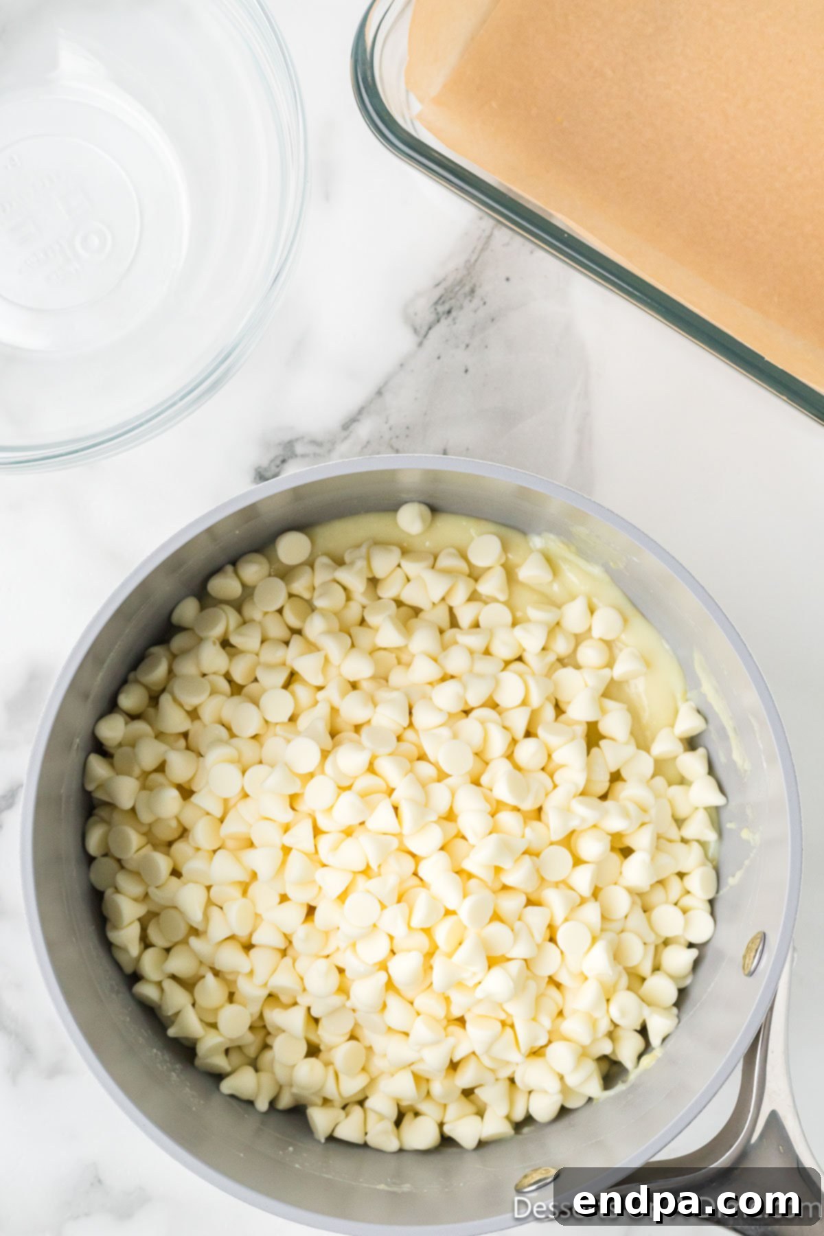 White chocolate chips being added to the warm lemon mixture in a saucepan.