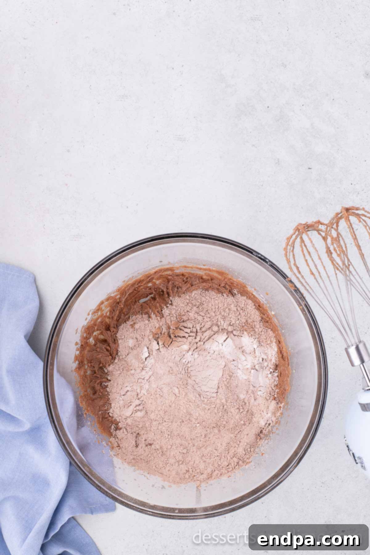 The wet and dry ingredients partially combined in a mixing bowl, showing the flour mixture gradually being incorporated into the butter mixture for the Nutella cookie dough.